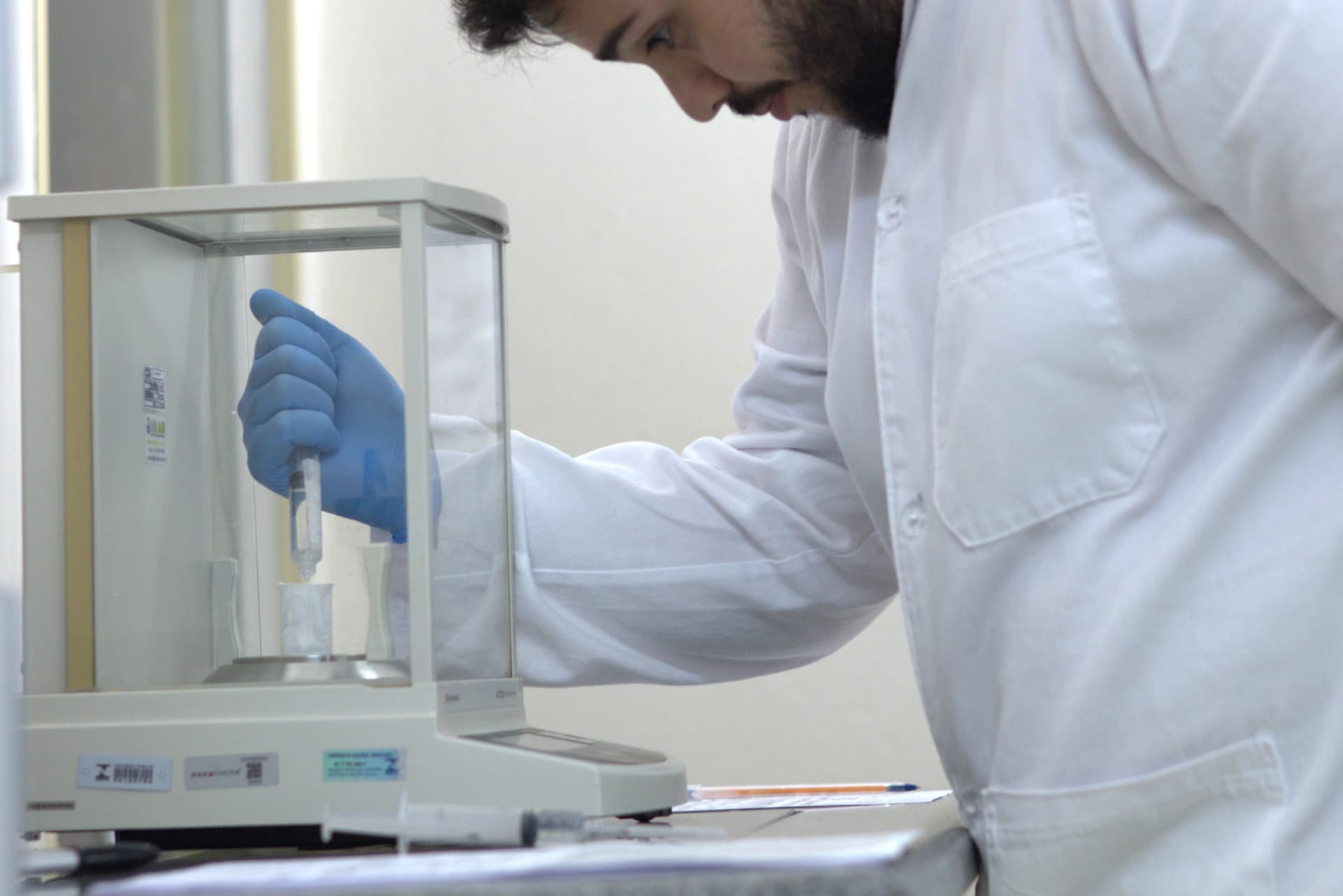 A imagem representa Estudos de Equivalência Química. Uma pessoa manipula um dispositivo de laboratório que está dentro de um equipamento, simbolizando a análise da equivalência do estado sólido e em solução. A imagem reflete o rigor e a precisão técnica na avaliação da similaridade entre diferentes produtos.