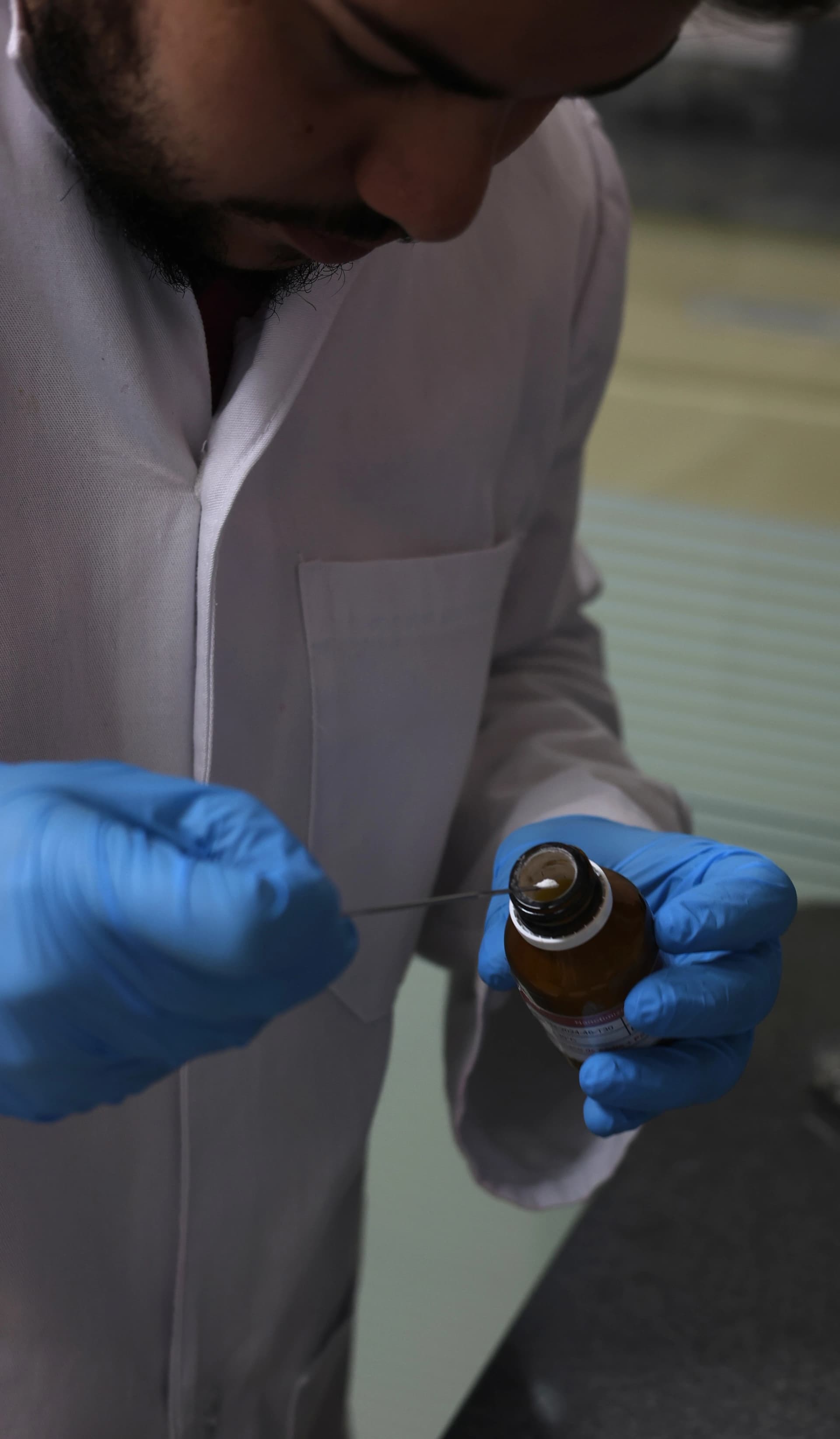 A imagem simboliza Estudos de Compatibilidade. Nela, uma pessoa de jaleco, em um laboratório, segura um frasco e retira uma porção de seu conteúdo em pó para análise. A imagem reflete a avaliação das interações entre princípios ativos e excipientes para garantir a estabilidade, a segurança e a eficácia do produto final.